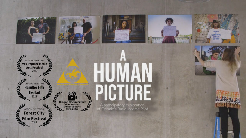 A Human Picture
A participatory exploration of Ontario's Basic Income Pilot. (a woman on the right standing on a ladder putting pictures on a gray concrete wall of people holding signs; there are five pictures already mounted. To the left is an overlay of various film awards, including "Official Selection Hamilton Film Festival 2023")