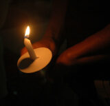 A lit candle with a cardboard wax catcher about halfway down.